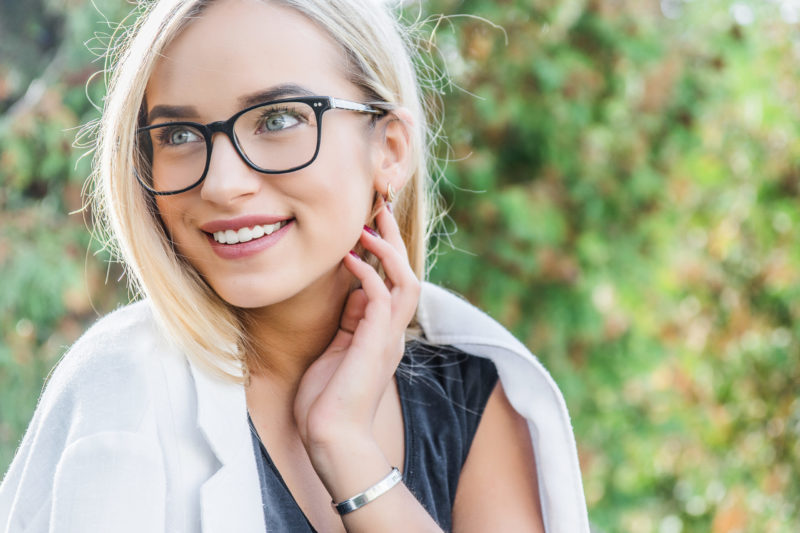 Retrato de una mujer joven rubia con gafas sonriendo en un parque