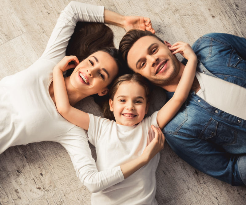 Vista superior de una niña y sus padres jóvenes mirando la cámara y sonriendo